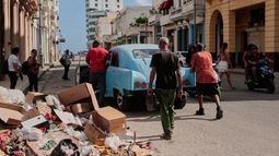 Varias personas empujan un coche clásico americano averiado junto a un montón de basura en La Habana, Cuba, el miércoles 17 de junio de 2026. (AP Foto/Jorge Luis Banos)
