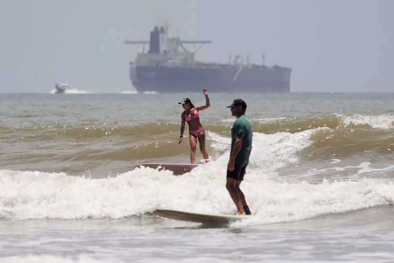 Un barco petrolero se dirige a aguas abiertas mientras los surfistas aprovechan las olas ante la llegada del huracán Beryl en Port Aransas, Texas, el sábado 6 de julio de 2024. (AP Foto/Eric Gay)