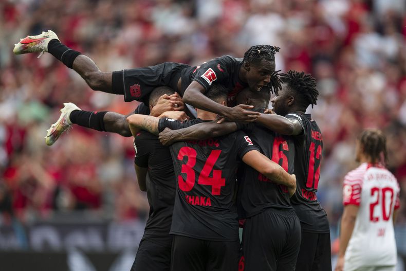 Jeremie Frimpong del Bayer Leverkusen salta sobre el goleador Jonathan Tah y sus compañeros tras el segundo gol de su equipo en el encuentro ante el Leipzig en la Bundesliga el sábado 19 de agosto del 2023. (Marius Becker/dpa via AP)