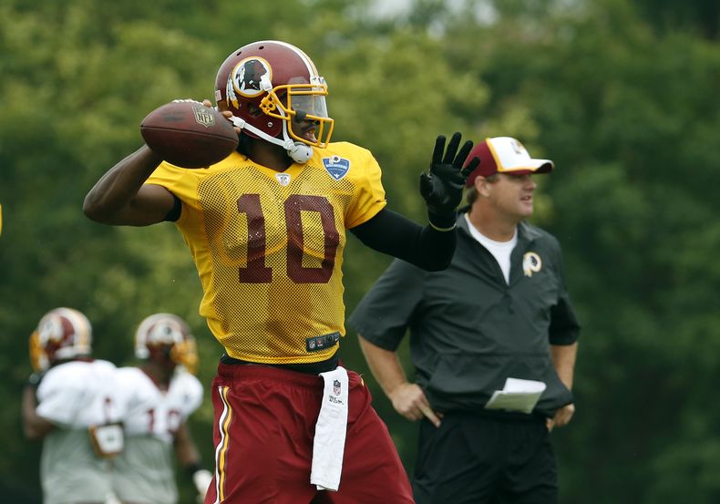 El jugador de los Redskins de Washington, Robert Griffin III, izquierda, lanza un pase en un entrenamiento el 27 de julio de 2014 en Roanoke, Virginia. (AP Photo/Alex Brandon, File)