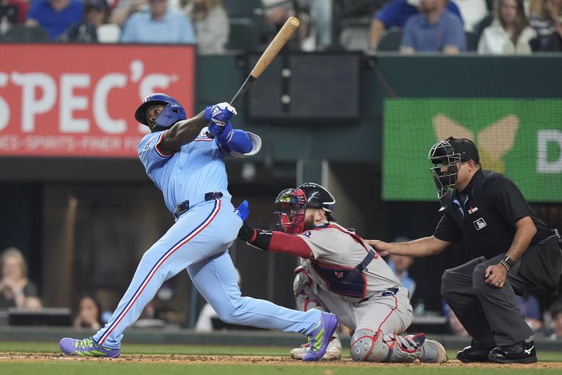 Adolis García, izquierda, de los Rangers de Texas, hace seguimiendo después de conectar un cuadrangular solitario frente a los Medias Rojas de Boston, ante las miradas del receptor Connor Wong, centro, y el umpire principal Néstor Ceja, derecha, durante la sexta entrada del juego de béisbol de las mayores, el domingo 30 de marzo de 2025, en Arlington, Texas. (AP Foto/LM Otero)