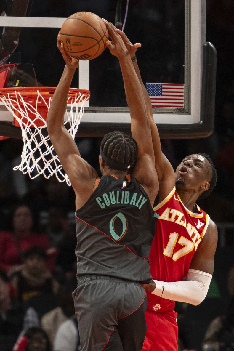 El escolta de los Wizards de Washington, Bilal Coulibaly (0), es bloqueado por el alero de los Hawks de Atlanta, Onyeka Okongwu (17), durante la segunda mitad del partido de baloncesto de la NBA, el sábado 13 de enero de 2024, en Atlanta. (AP Foto/Hakim Wright Sr.)
