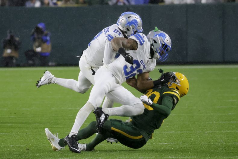 El cornerback de los Lions de Detroit, Amik Robertson (21) y el safety, Brian Branch (32) son penalizados por rudeza innecesaria luego de taclear al wide receiver de los Packers de Green Bay, Bo Melton durante la primera mitad del juego de la NFL el domingo 3 de noviembre de 2024, en Green Bay, Wisconsin. (AP Foto/Mike Roemer)
