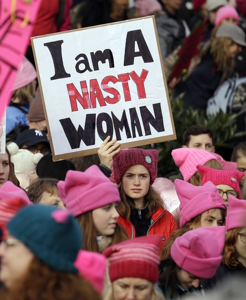 ARCHIVO - Una mujer con un letrero en medio de una ola de gorros rosados antes de la marcha de las mujeres con más de 100.000 participantes el 21 de enero de 2017, en Seattle. Las mujeres marcharon en solidaridad con la Marcha de las Mujeres en Washington para apoyar las causas de las mujeres. La influencia simbiótica del color rosado, con el impulso de una fuerza cultural, fue evidente en 2017 en la Marcha de las Mujeres en Washington, donde las manifestantes se pusieron gorros de gatito de color rosa vibrante. (Foto AP/Elaine Thompson, archivo)