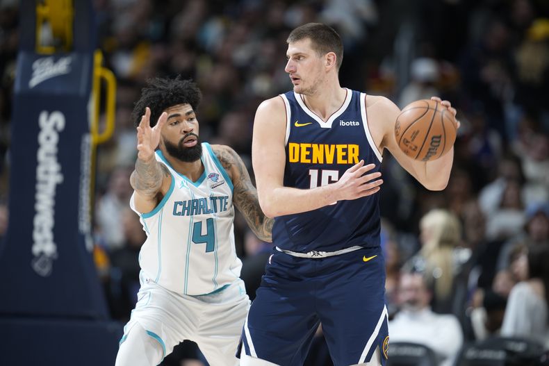 Nikola Jokic, derecha, pívot de los Nuggets de Denver, busca pasar el balón mientras que Nick Richards (4), de los Hornets de Charlotte, defiende en la segunda mitad del juego de baloncesto de la NBA, el lunes 1 de enero de 2024, en Denver. (AP Foto/David Zalubowski)