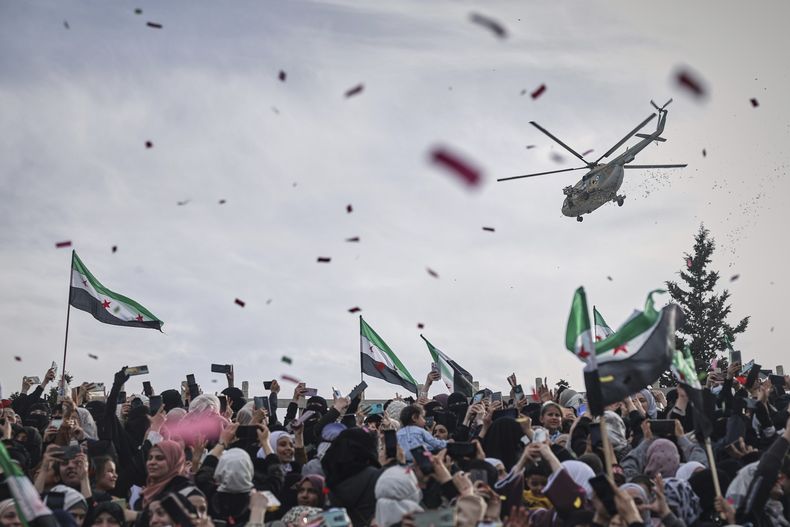 Un helicóptero militar arroja confeti y flores sobre una multitud durante la celebración del 10mo aniversario de la victoria de las fuerzas rebeldes sobre el ejército de Bashar al-Assad en Idlib, Siria, el viernes 28 de marzo de 2025. (AP Foto/Ghaith Alsayed)