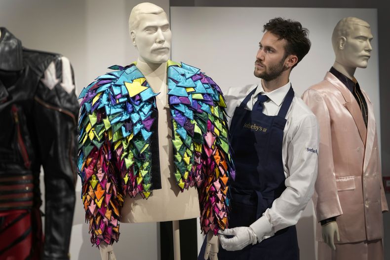 Un empleado de Sothebys muestra una chaqueta con apliques de flechas de satén de color arcoiris de 1982 en las salas de la casa de subastas de Sothebys en Londres, el jueves 3 de agosto de 2023.Más de 1.400 artículos personales de Freddie Mercury, incluidos sus extravagantes vestuarios, borradores escritos a mano de Bohemian Rhapsody y el piano de media cola que usó para componer los grandes éxitos de Queen, se exhibirán en la casa de subastas Sothebys Londres antes de su venta. (Foto AP/Kirsty Wigglesworth)