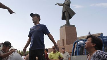 ARCHIVO - Vecinos locales de origen kirguís y uzbeco reciben ayuda humanitaria ante una estatua del fundador de la Unión Soviética, Vladimir Lenin, en una plaza central de la ciudad de Osh, en el centro de Kirguistán, el martes 22 de junio de 2010. (AP Foto/Sergei Grits, Archivo)