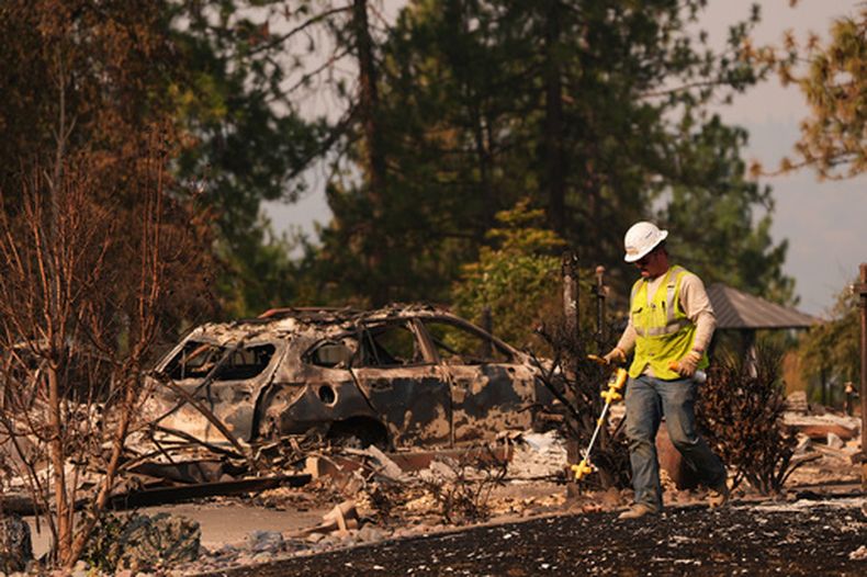 Un trabajador de Avista se mueve por un terreno tras un incendio en el norte de Spokane, Washington, el lunes 3 de agosto de 2026. (AP Foto/Lindsey Wasson)