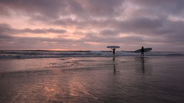 Surfistas entran en el océano Pacífico al atardecer, el jueves 1 de octubre de 2026 en Encinitas, California. (AP Foto/Gregory Bull)