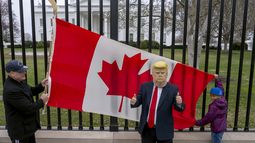 Los residentes de Toronto, Douglas Bloomfield (izquierda) y su hijo Phoenix (derecha), quienes están de vacaciones en Washington, sostienen una bandera canadiense y un palo de hockey para mostrar su apoyo a Canadá mientras otra persona que también se encuentra visitando la ciudad porta una máscara del presidente Donald Trump, frente a la Casa Blanca, el jueves 13 de marzo de 2025. (AP Foto/Ben Curtis)