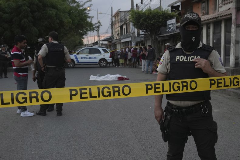 ARCHIVO - Un policía resguarda una escena del crimen donde aún permanece el cuerpo de un hombre, asesinado en circunstancias desconocidas, cubierto por una sábana en una calle de Durán, Ecuador, el viernes 21 de julio de 2023. El costo humano de la transformación de Ecuador en un gran centro de tráfico de drogas ha sido inmenso, según se refleja en el aumento récord de muertes violentas en 2022, con 4.600 asesinatos, el doble que el año anterior. (AP Foto/Dolores Ochoa, Archivo)