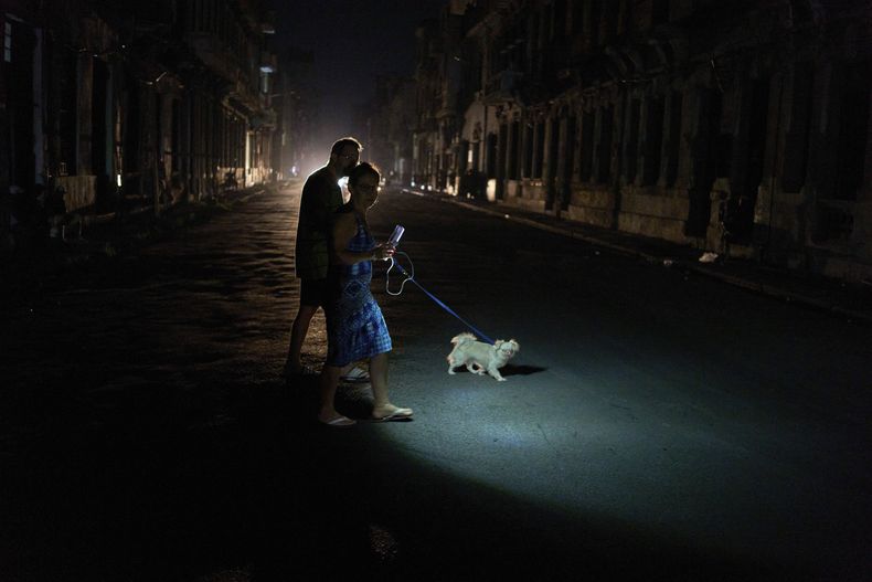 La gente enciende una linterna mientras cruza una calle con su perro durante un apagón en La Habana, el miércoles 10 de septiembre de 2025. (AP Foto/Ramón Espinosa)