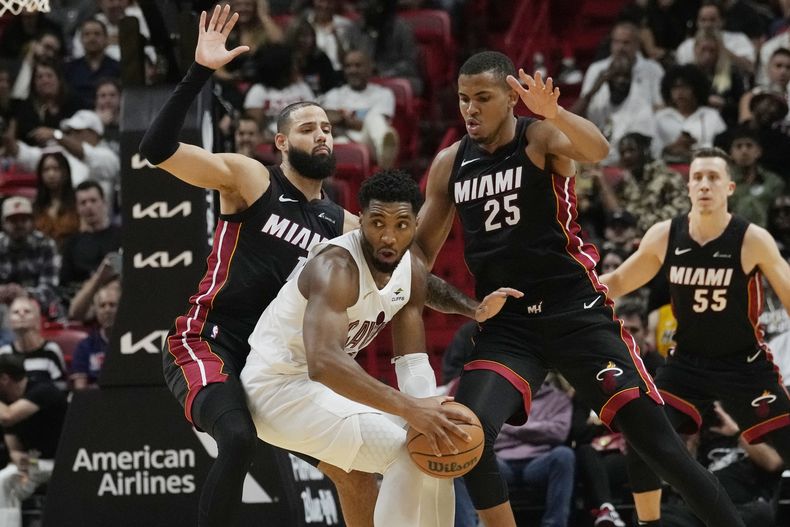 El escolta del Heat de Miami Caleb Martin (16) y el centro Orlando Robinson (25) defienden ante el base de los Cavaliers de Cleveland Donovan Mitchell durante la segunda mitad del juego de NBA, el viernes 8 de diciembre de 2023, en Miami. (AP Foto/Marta Lavandier)
