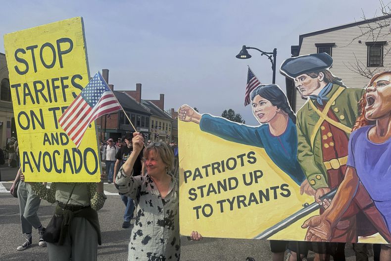 Un grupo de manifestantes sostiene letreros en un desfile para conmemorar el 250mo aniversario de la Guerra de Independencia de Estados Unidos, el sábado 19 de abril de 2025, en Concord, Massachusetts. (AP Fotos/Michael Casey)