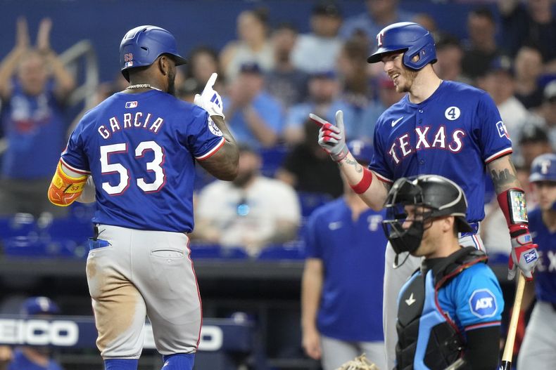 Adolis García (53), de los Rangers de Texas, se encuentra con Jonah Heim, derecha, después de anotar con un jonrón solitario durante la sexta entrada del juego de béisbol en contra de los Marlins de Miami, el domingo 2 de junio de 2024, en Miami. (AP Foto/Lynne Sladky)