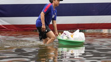 Una mujer vadea zonas inundadas ante una bandera nacional tras fuertes lluvias en Bangkok, Tailandia, el domingo 27 de septiembre de 2026. (AP Foto/Sakchai Lalit)