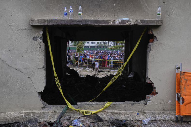 Gente mirando vista a través de la ventana de una clase quemada en un edificio escolar, después de que un avión militar de entrenamiento se estrellara el lunes en Daca, Bangladesh, el martes 22 de julio de 2025. (AP Foto/Mahmud Hossain Opu)