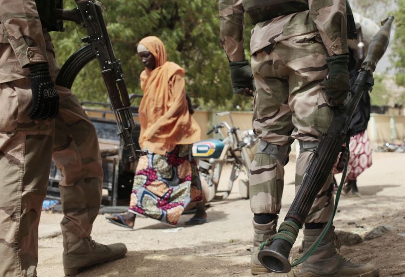 ARCHIVO - Una mujer pasa junto a soldados nigerianos en un puesto de control en Gwoza, Nigeria, una ciudad recién liberada de Boko Haram, miércoles 8 de abril de 2015. (AP foto/Lekan Oyekanmi, archivo)