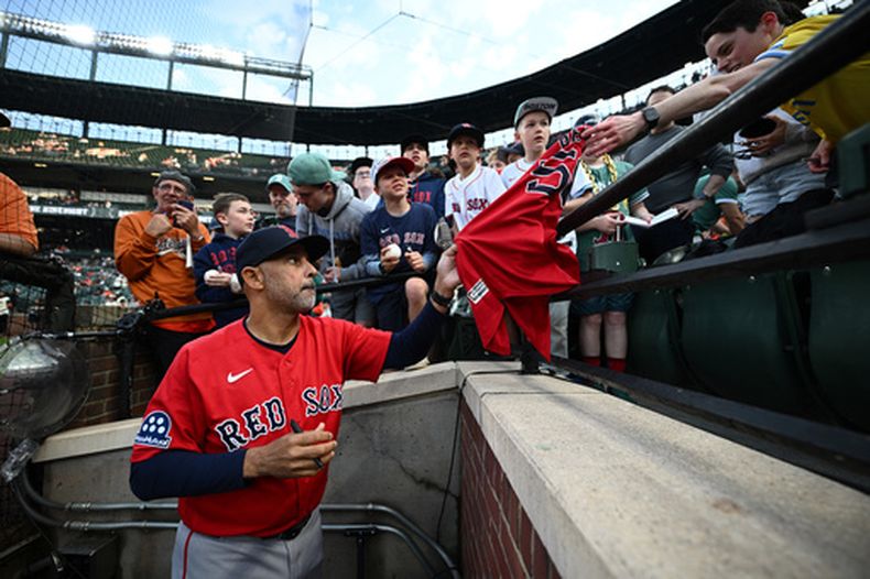 El mánager de los Medias Rojas de Boston, Alex Cora, en primer plano, firma autógrafos para los aficionados antes de un partido de béisbol contra los Orioles de Baltimore, el viernes 24 de abril de 2026, en Baltimore. (AP Foto/Nick Wass)