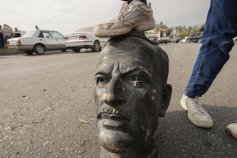 Un combatiente de oposición pone su pie sobre el busto del difunto presidente sirio Hafez Assad en Damasco, Siria, el domingo 8 de diciembre de 2024. (AP Foto/Hussein Malla)