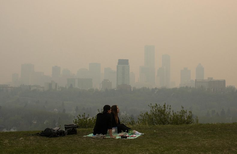 El humo de incendios forestales envuelve la ciudad mientras una pareja toma un picnic en Edmonton, Alberta, el sábado 11 de mayo de 2024. (Jason Franson/The Canadian Press via AP)