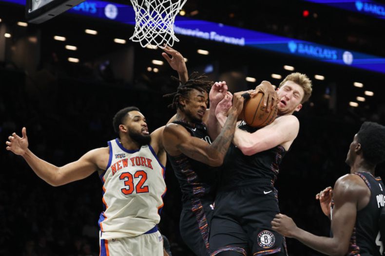 Nic Claxton, izquierda, y su compañero Danny Wolf, derecha, de los Nets de Brooklyn, ambos pelean un rebote ante la mirada de Karl-Anthony Towns (32), de los Knicks de Nueva York, durante la segunda mitad del juego de baloncesto de la NBA, el viernes 20 de marzo de 2026, en Nueva York. (AP Foto/Heather Khalifa)