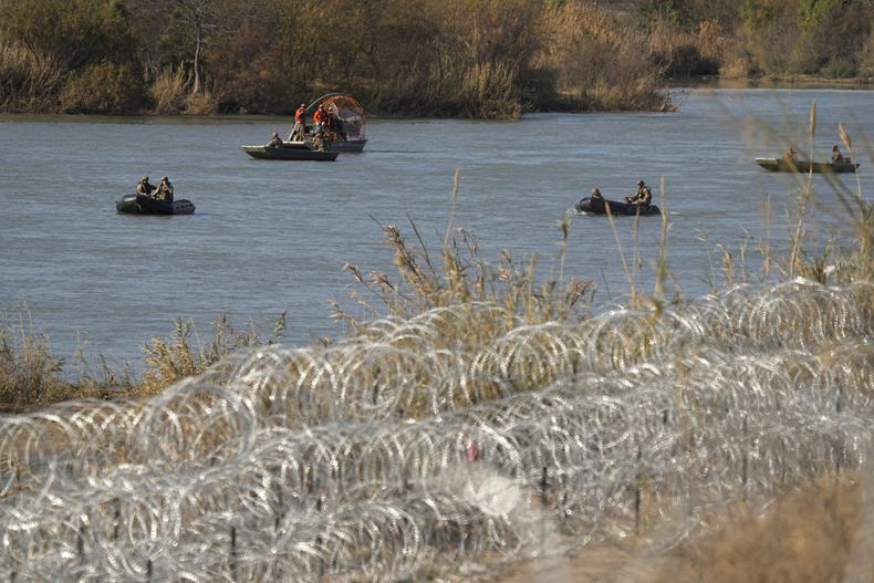 Guardas que patrullan el río Bravo en pequeñas embarcaciones pasan junto a filas de alambre con concertinas, instaladas para ayudar a frenar los cruces ilegales, el 1 de febrero de 2024, en Eagle Pass, Texas. (AP Foto/Eric Gay)