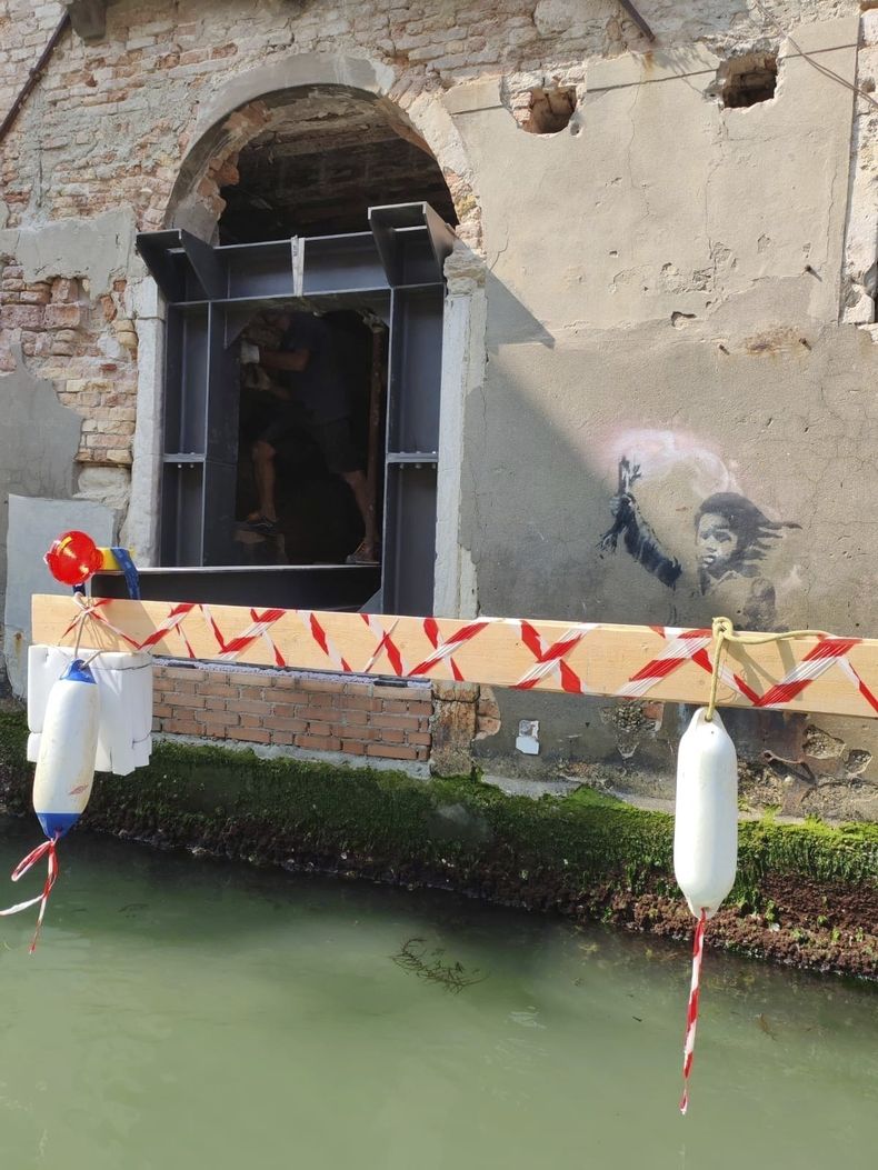 En esta imagen proporcionada jueves 24 de julio de 2025, la obra de Banksy The Migrant Child es retirada de la fachada del Palazzo San Pantalon en Venecia, Italia, para completar su rescate. (Ifis Art Via AP)