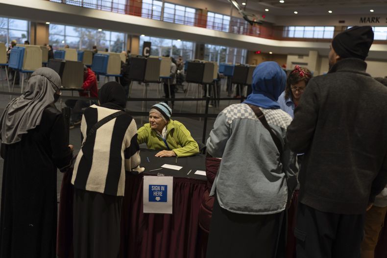 La funcionaria electoral Marjorie Pasqualle, en el centro, ayudar a los votantes a registrarse en el centro Ford Community and Performing Arts el último día para el voto adelantado, el domingo 3 de noviembre de 2024, en Dearborn, Michigan. (AP Foto/David Goldman)