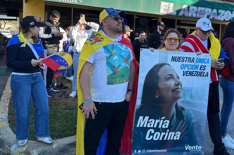 De izquierda a derecha, los venezolanos David Núñez, Lisbeth García y Víctor Giménez se reúnen fuera del restaurante El Arepazo con un cartel de la líder opositora y ganadora del Premio Nobel de la Paz María Corina Machado en las celebraciones por la captura del presidente venezolano Nicolás Maduro en Doral, Florida, el sábado 3 de enero de 2026. (AP Foto/Vanessa Alvarez)