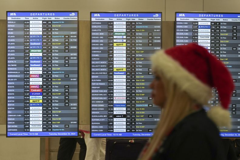 Una empleada con un gorro de Santa Claus camina frente a unas pantallas que muestran vuelos demorados en la terminal de American Airlines del Aeropuerto Internacional de Miami en la Nochebuena, el martes 24 de diciembre de 2024. (AP Foto/Rebecca Blackwell)