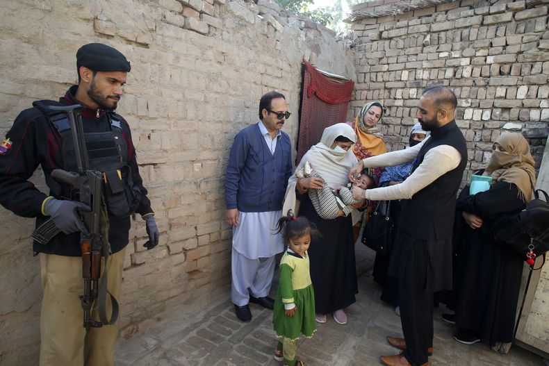 Un policía monta guardia mientras un trabajador de salud administra una vacuna contra la polio a un niño en Peshawar, Pakistán, el lunes 16 de diciembre de 2024. (AP Foto/Muhammad Sajjad)