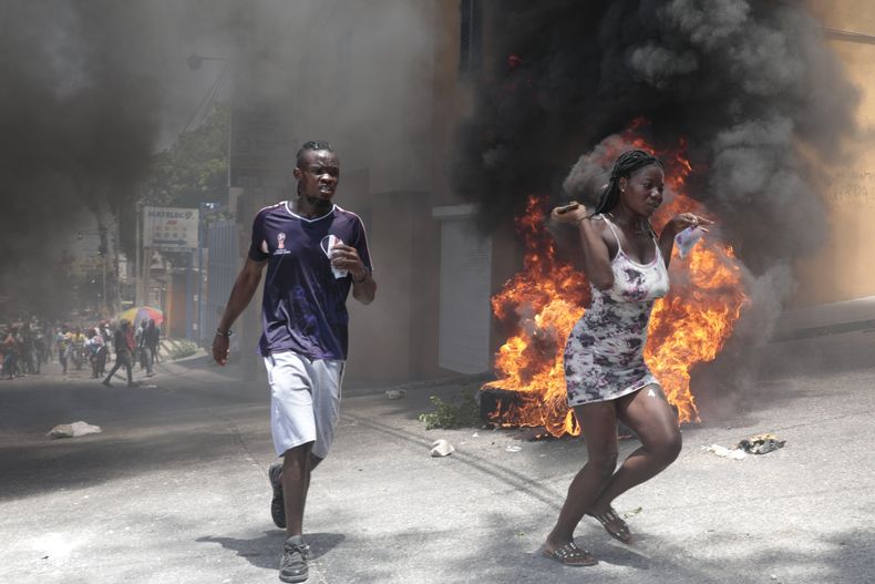 Manifestantes pasan corriendo junto a neumáticos incendiados durante una protesta contra la inseguridad, el 7 de agosto de 2023, en Puerto Príncipe, Haití. (Foto AP/Odelyn Joseph)