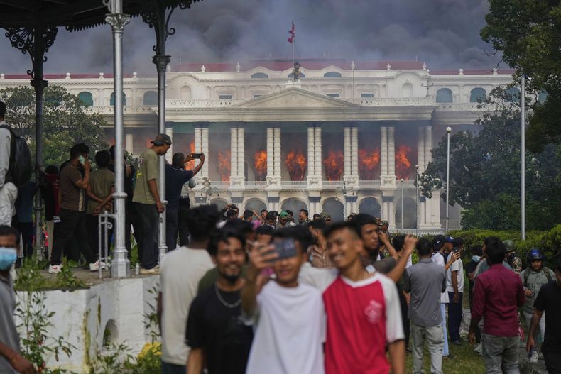Manifestantes se toman selfies y celebran frente al Singha Durbar, sede de varias agencias y oficinas del gobierno de Nepal, después de que manifestantes le prendieron fuego durante una protesta contra los bloqueos a las redes sociales y a la corrupción en el país, el martes 9 de septiembre de 2025, en Katmandú, Nepal. (AP Foto/Niranjan Shrestha)