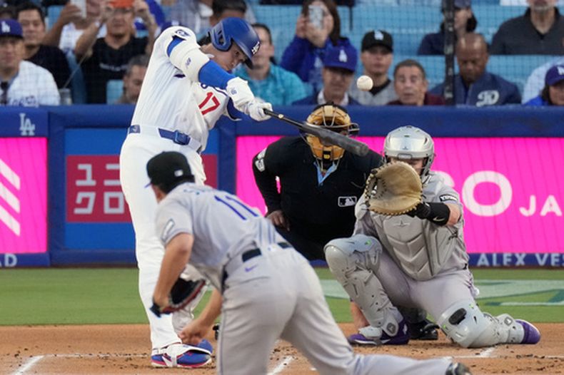 Shohei Ohtani (17), de los Dodgers de Los Ángeles, conecta un jonrón solitario ante Tomoyuki Sugano (11), lanzador de los Rockies de Colorado, mientras el receptor, Hunter Goodman, observa durante la primera entrada del juego de béisbol de Grandes Ligas, el miércoles 27 de mayo de 2026, en Los Ángeles. (AP Foto/Mark J. Terrill)