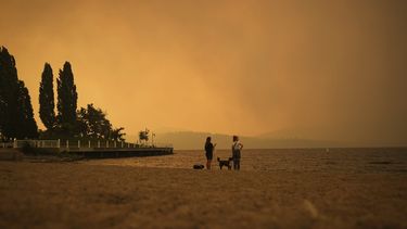ARCHIVO - El humo del incendio de McDougall Creek llena el aire mientras dos personas miran el paisaje en el lago Okanagan desde la playa Tugboat, en Kelowna, Columbia Británica. Los catastróficos incendios forestales del año pasado impulsados por el cambio climático en Canadá expulsaron más dióxido de carbono que atrapa el calor en la atmósfera de lo que emitió India con la quema de combustibles fósiles, al consumir una zona de bosque más grande que Virginia Occidental, según una nueva investigación. (Darryl Dyck/The Canadian Press via AP, Archivo)