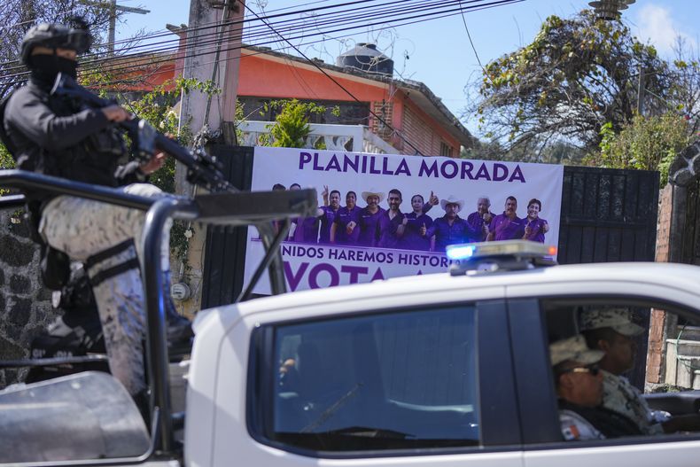 Agentes de la Guardia Nacional de México pasan en un vehículo por delante de un cartel en el que aparecen las cinco personas asesinadas el día anterior, en Huitzilac, México, el martes 14 de enero de 2025. (AP Foto/Fernando Llano)