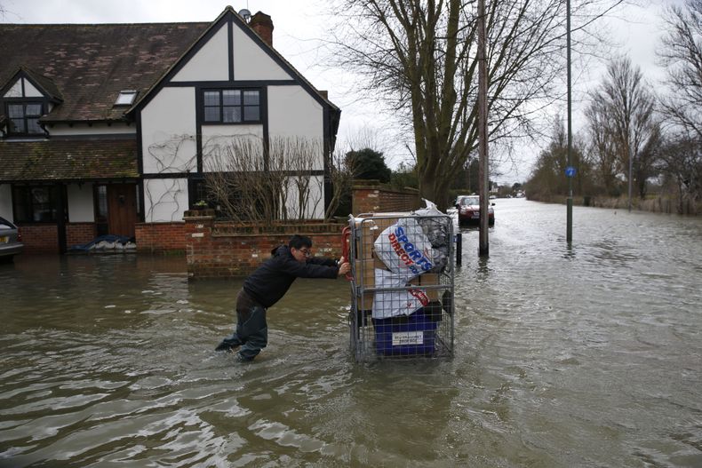 Un residente local empuja un carrito con algunas pertenencias en &eacute;l en la parte inundada por tormentas del poblado Staines-upon-Thames, Inglaterra, mientras un veh&iacute;culo policial patrulla el &aacute;rea, el mi&eacute;rcoles 12 de febrero de 2