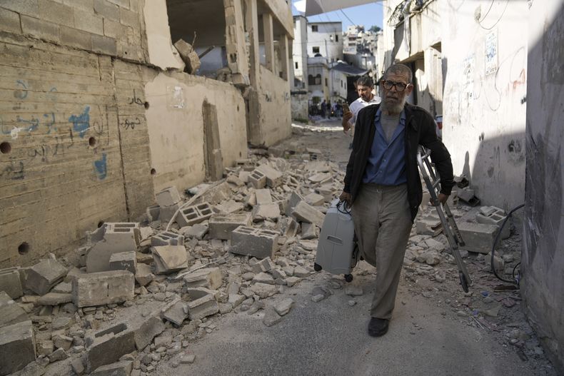 Palestinos caminan junto a una casa dañada en el campamento de refugiados Jenin en Cisjordania, el miércoles 5 de julio de 2023, después de que el ejército israelí retirara sus fuerzas del baluarte miliciano. (AP Foto/Nasser Nasser)
