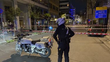 Un policía monta guardia tras la explosión de una presunta bomba fuera de las oficinas de Hellenic Train, la empresa que dirige el ferrocarril griego, el tercer edificio a la izquierda, en Atenas, Grecia, el viernes 11 de abril de 2025. (AP Foto/Derek Gatopoulos)