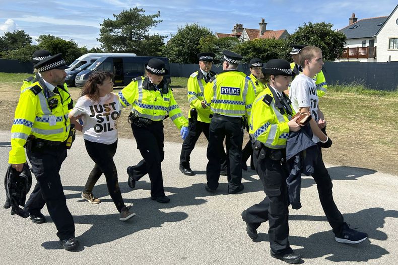 Manifestantes de Just Stop Oil son escoltados por la policía en el hoyo 17 después de que lanzaron un material naranja al campo en el Abierto Británico el viernes 21 de julio del 2023. (AP Foto)
