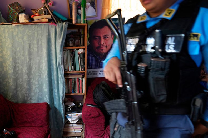 ARCHIVO - Un cartel del ambientalista asesinado Juan López cuelga en su casa mientras un guardaespaldas estatal vigila a la familia López en Tocoa, Honduras, el 6 de diciembre de 2024. (AP Foto/Moisés Castillo, Archivo)
