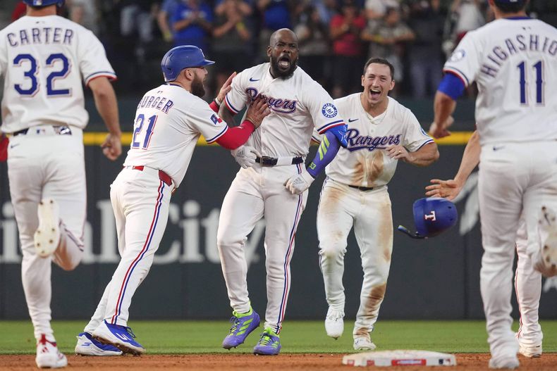 El cubano Adolis García (centro), celebra con sus compañeros de los Rangers de Texas, luego de producir la carrera del triunfo sobre los Medias Blancas de Chicago, el sábado 14 de junio de 2025 (AP Foto/LM Otero)