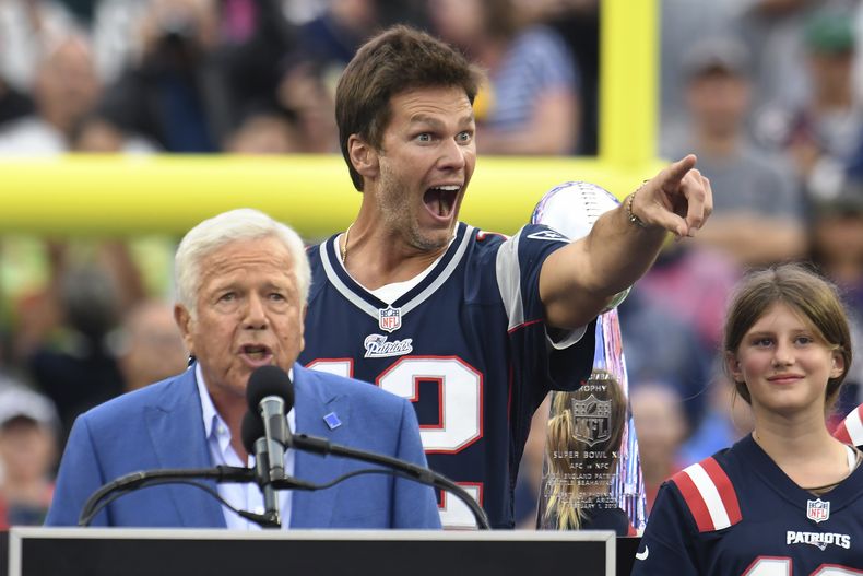 Tom Brady, atrás, quien fuera quarterback de los Patriots de Nueva Inglaterra, señala hacia los fanáticos mientras el dueño del equipo, Robert Kraft, izquierda, habla y la hija de Brady, Vivian, derecha, observa durante la ceremonia de medio tiempo, para honrar a Brady en el partido de la NFL entre los Eagles de Filadelfia y los Patriots, el domingo 10 de septiembre de 2023, en Foxborough, Massachusetts. (AP Foto/Mark Stockwell)