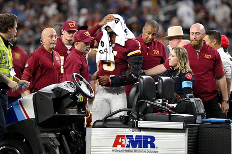 Los entrenadores atienden al quarterback de los Commanders de Washington, Jayden Daniels (5), tras una aparente lesión en la primera mitad contra los Cowboys de Dallas durante un partido de fútbol americano de la NFL en Arlington, Texas, el domingo 20 de septiembre de 2026. (Foto AP/Jessica Tobias)