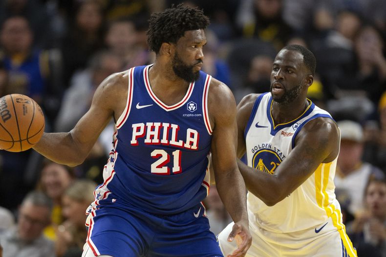 El pívot de los 76ers de Filadelfia Joel Embiid observa antes de pasar el balón mientras lo defiende el alero de los Warriors de Golden State Draymond Green en el encuentro del martes 30 de enero del 2024. (AP Foto/D. Ross Cameron)
