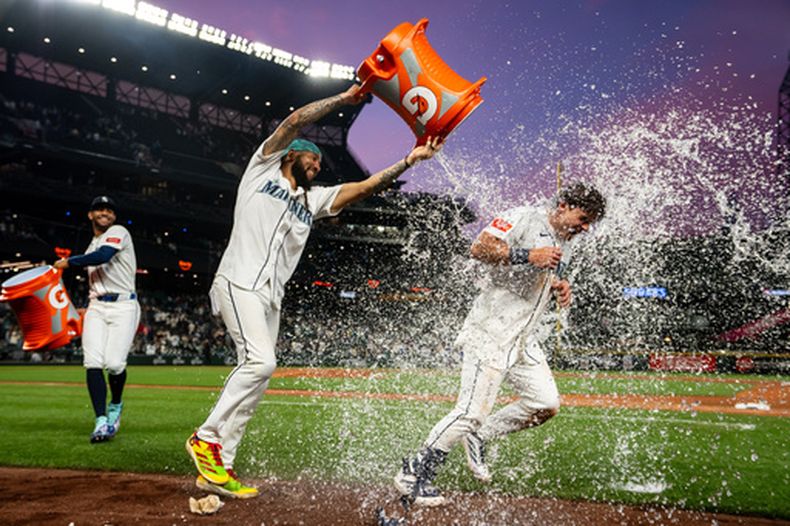 J.P. Crawford, centro, y Julio Rodríguez, izquierda, bañan a Cole Young después del partido de béisbol de Grandes Ligas frente a los Mets de Nueva York, el lunes 1 de junio de 2026, en Seattle. (AP Foto/Stephen Brashear)