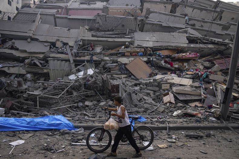 Un niño palestino camina con una bicicleta junto a los restos de un edificio alcanzado por un ataque aéreo israelí en Ciudad de Gaza, el domingo 8 de octubre de 2023. Los milicianos de Hamas, que controlan la Franja de Gaza, hicieron un ataque sin precedentes desde varios frentes al amanecer del sábado en el que docenas de combatientes de Hamas cruzaron la fortificada frontera y atacaron varios lugares, donde mataron a cientos de personas y tomaron rehenes. Las autoridades palestinas de salud reportaron decenas de muertes en los ataques aéreos israelíes en Gaza. (AP Foto/Fatima Shbair)