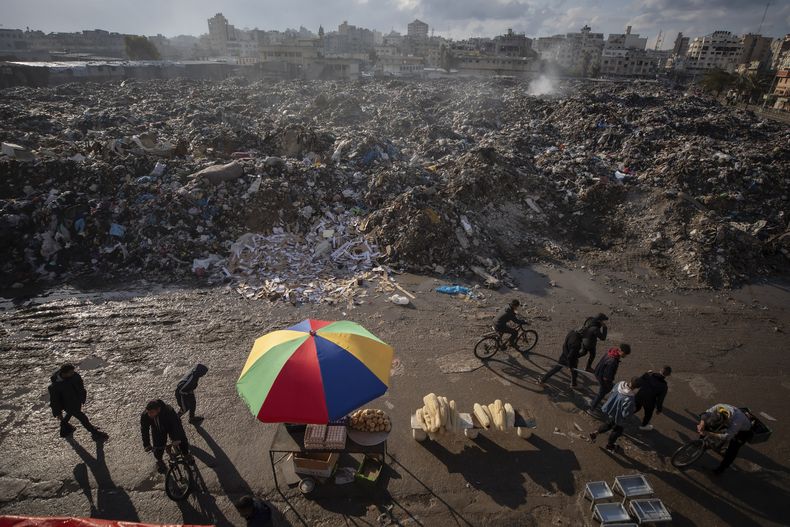 Palestinos pasan junto a montones de basura ardiendo en la Ciudad de Gaza, que no cuenta con sistema de recogida de basuras, el 12 de febrero de 2025. (AP Foto/Jehad Alshrafi)